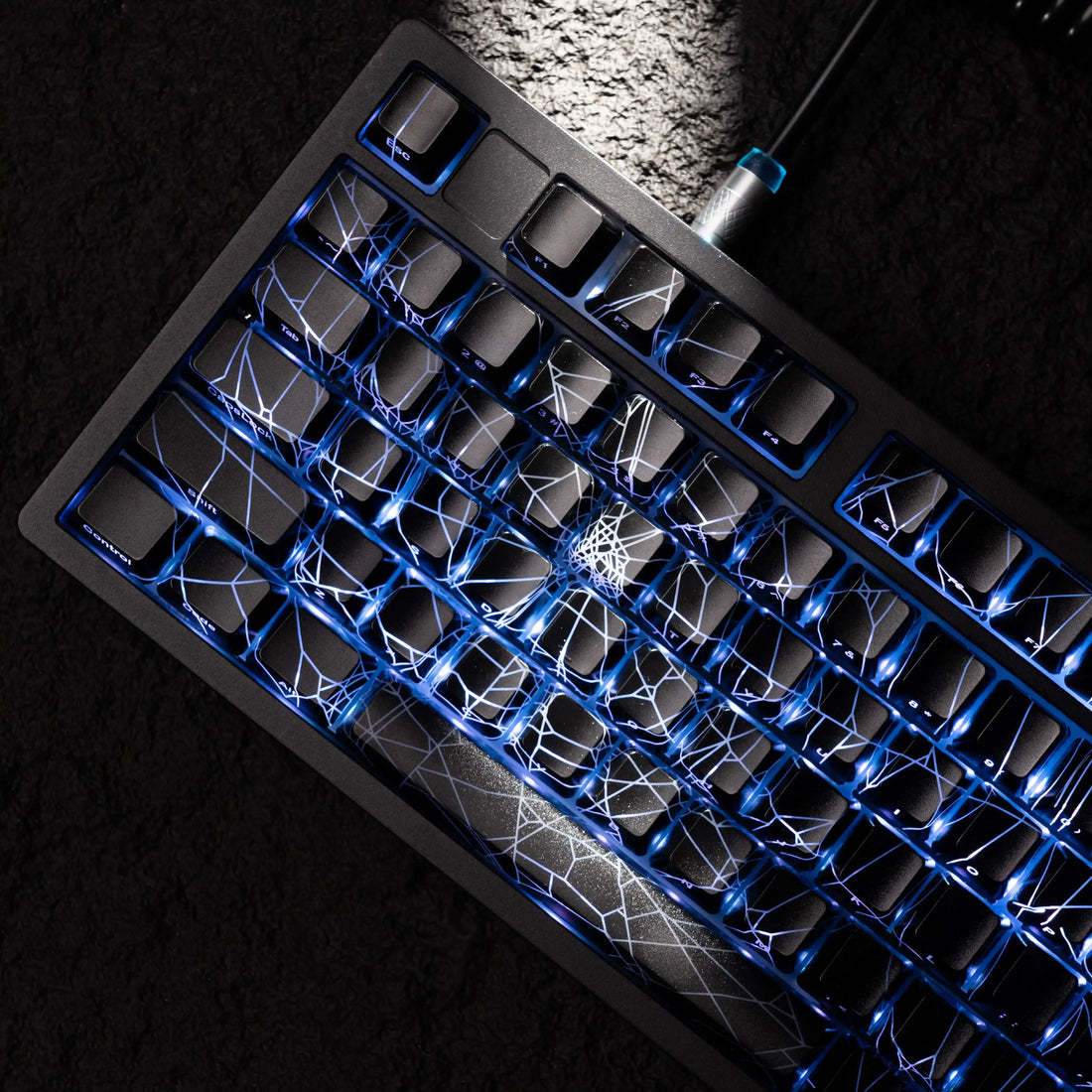 Black mechanical keyboard with blue LED backlighting and white spider web design on keys