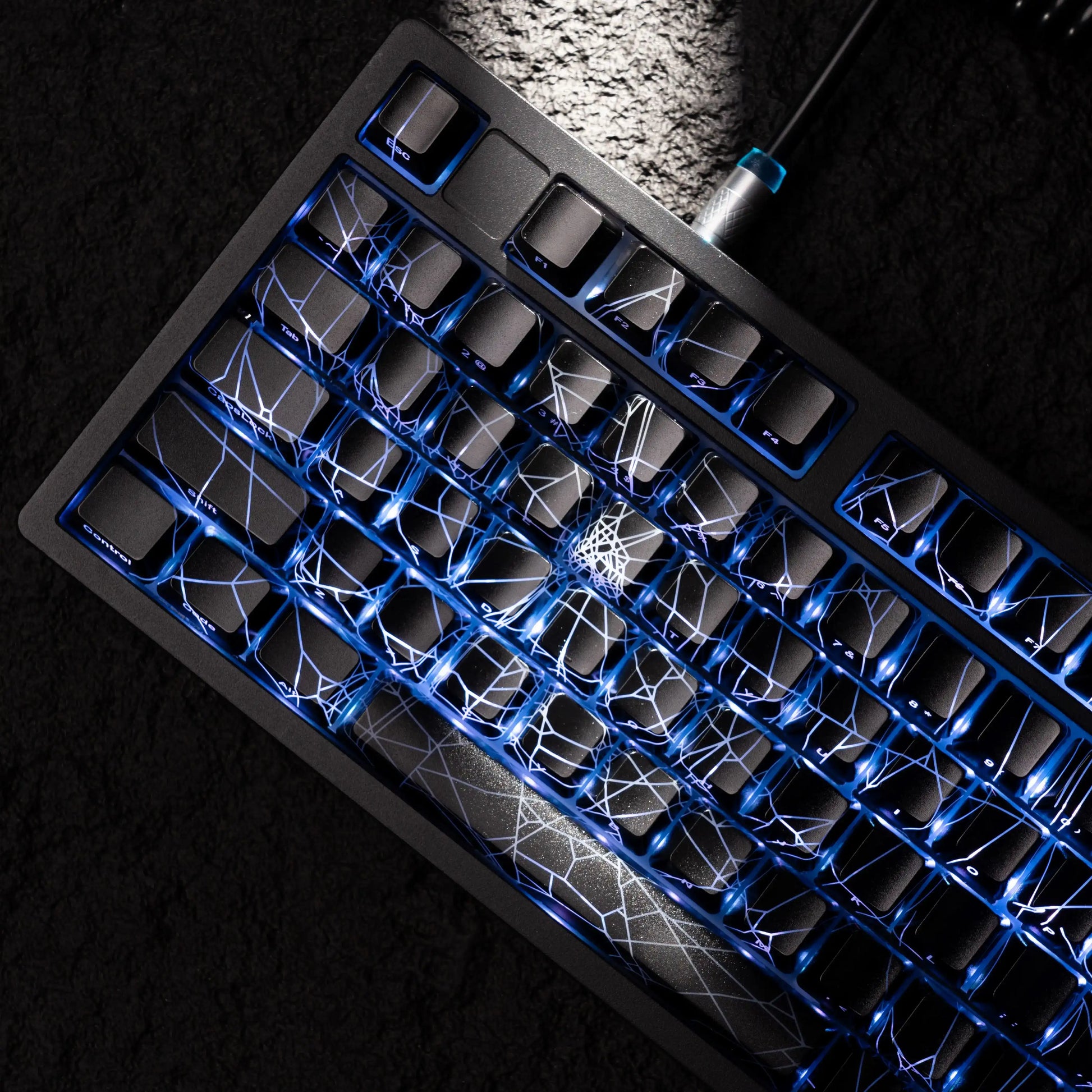 Black mechanical keyboard with blue LED backlighting and white spider web design on keys