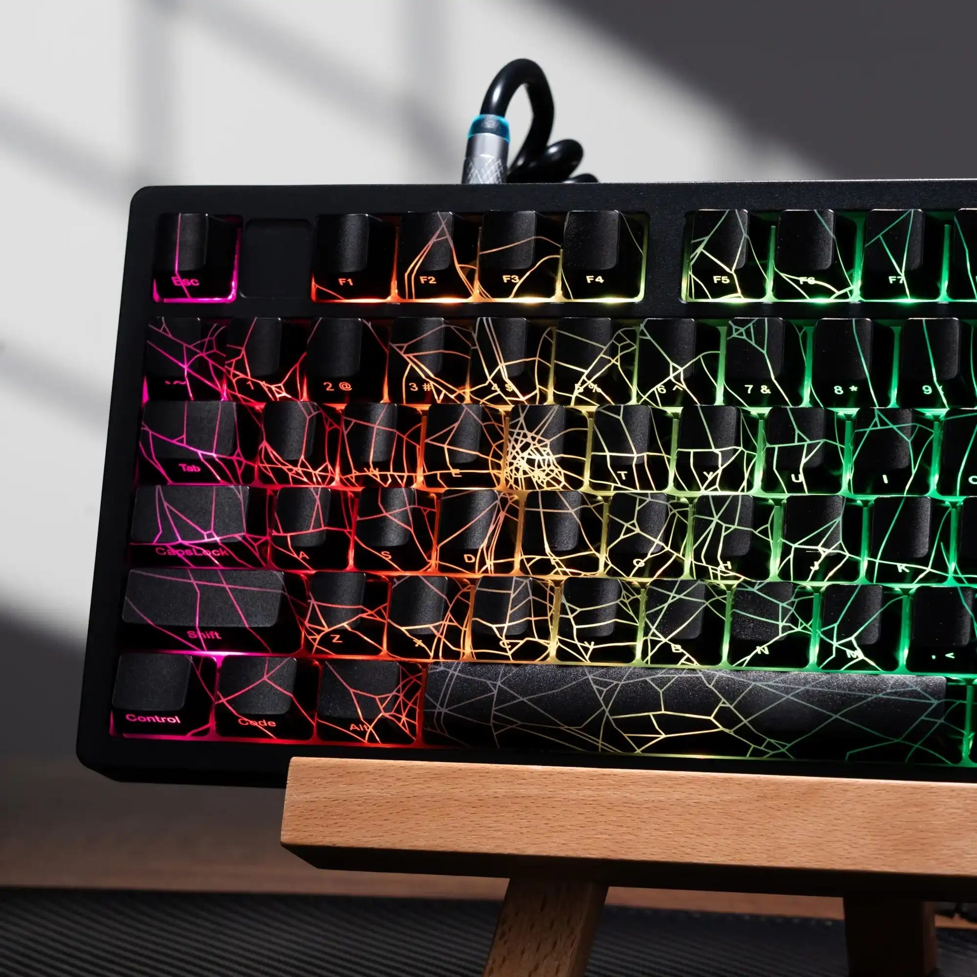 Mechanical keyboard with RGB backlighting and spiderweb pattern on black keycaps, on wooden stand